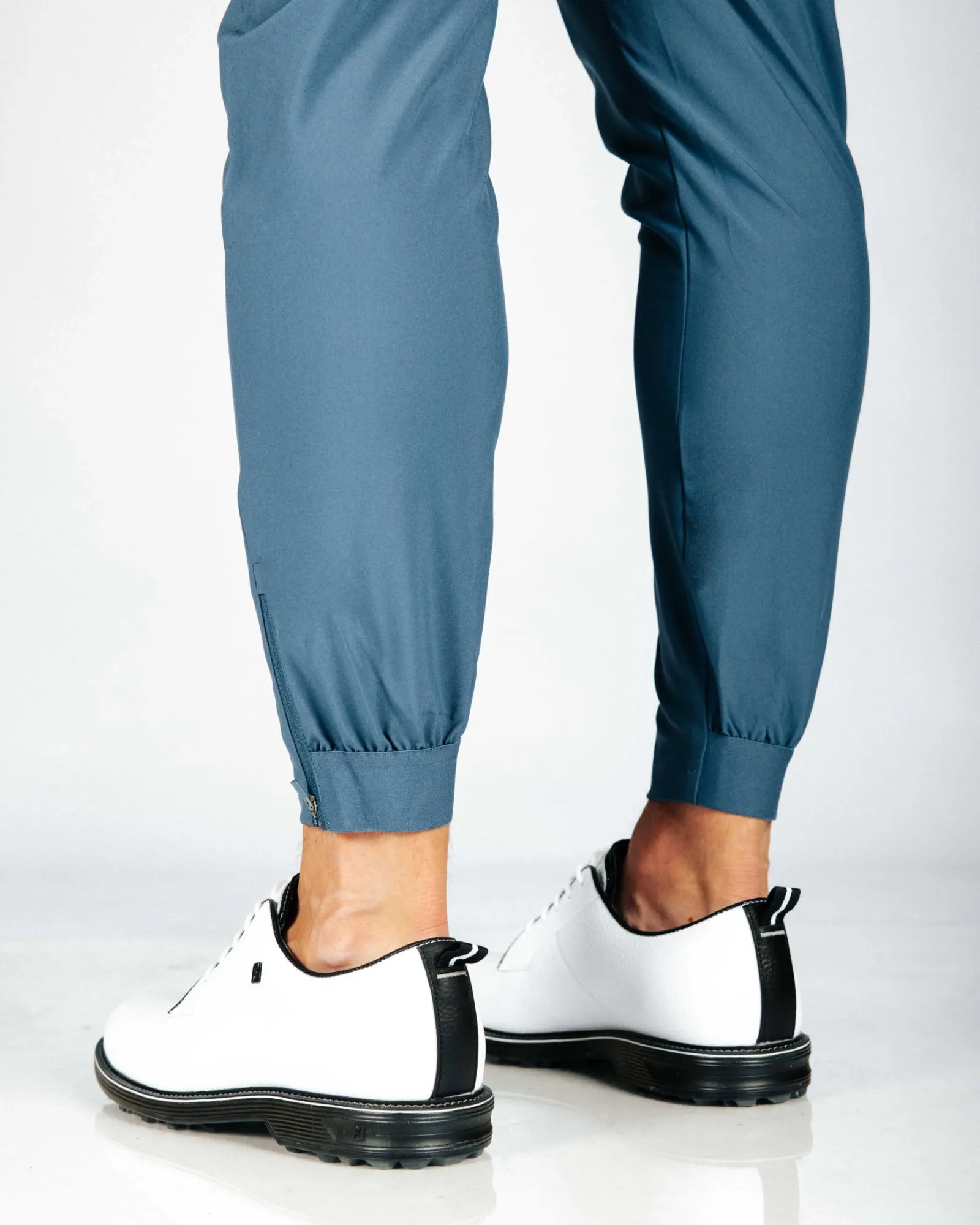 Person wearing blue pants and white sneakers with black soles on a light gray background