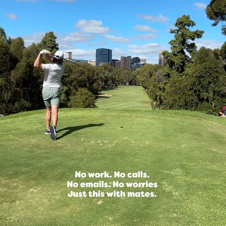 Person playing golf on a green course with trees and buildings in the background