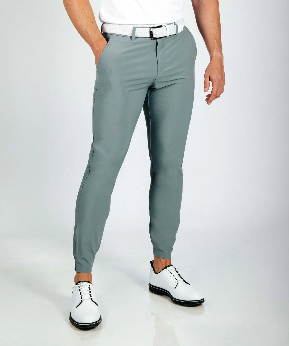 Person wearing smoke green golf pants and white shoes on a light gray background