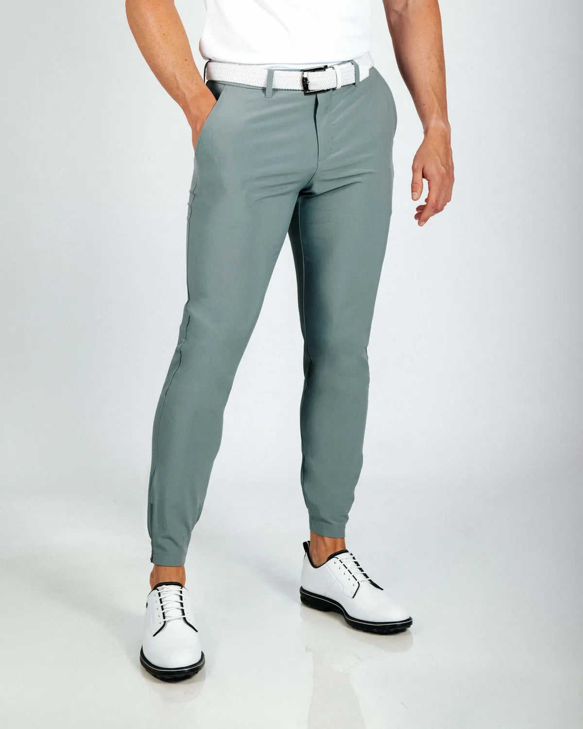 Person wearing smoke green golf pants and white shoes on a light gray background