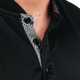 Close-up of a black polo with mock collar and patterned button placket.