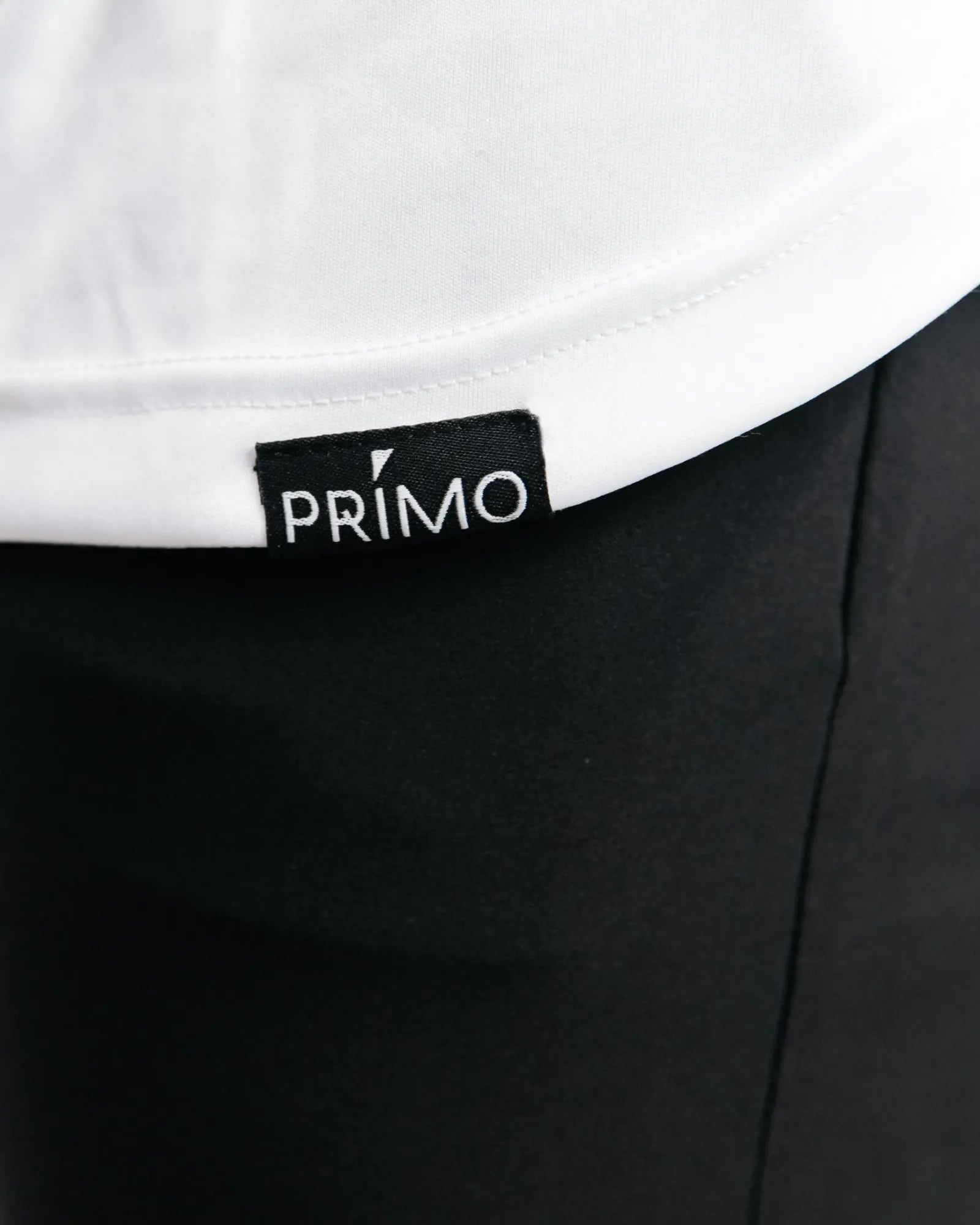 Close-up of a black garment with a Primo label on a white background