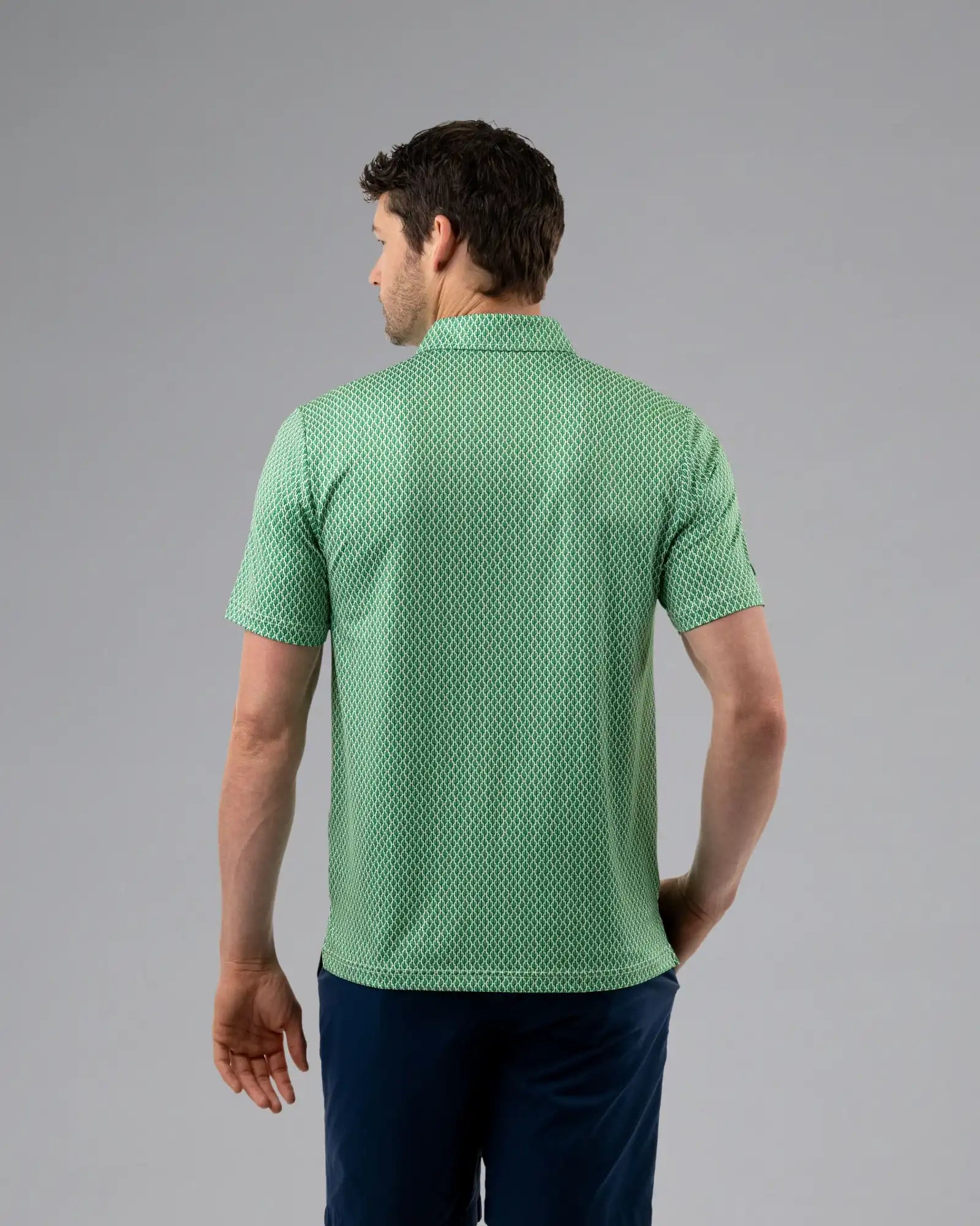 Man wearing a green patterned polo shirt on a gray background
