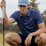 Man on golf course wearing a light blue cap with the brand 'Good Good' on the front.