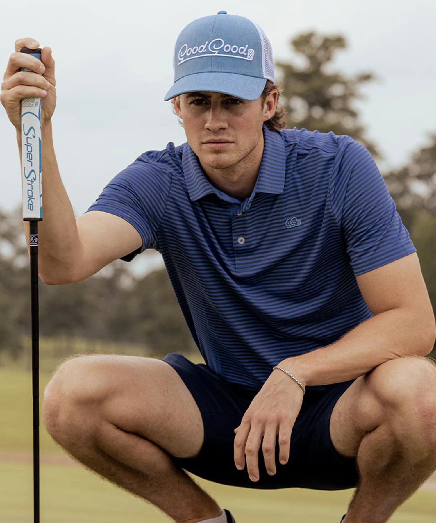 Man on golf course wearing a light blue cap with the brand 'Good Good' on the front.