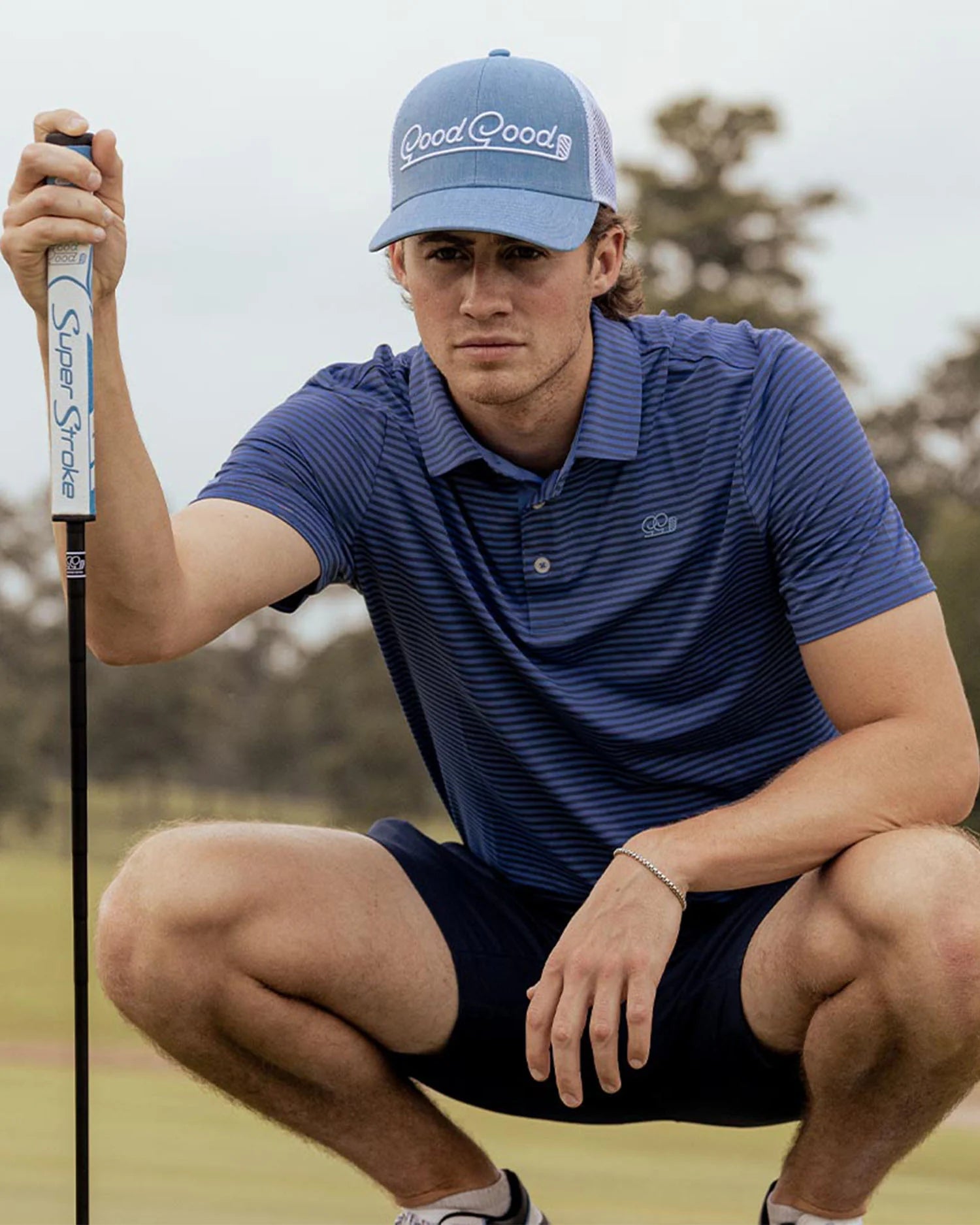 Man on golf course wearing a light blue cap with the brand 'Good Good' on the front.