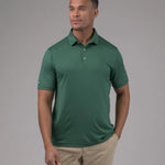 Man wearing a green polo shirt and beige pants against a gray background