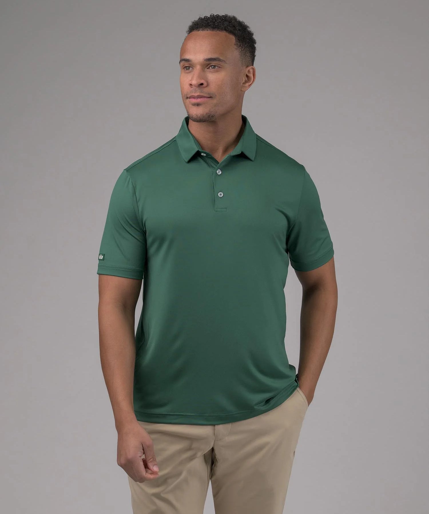 Man wearing a green polo shirt and beige pants against a gray background