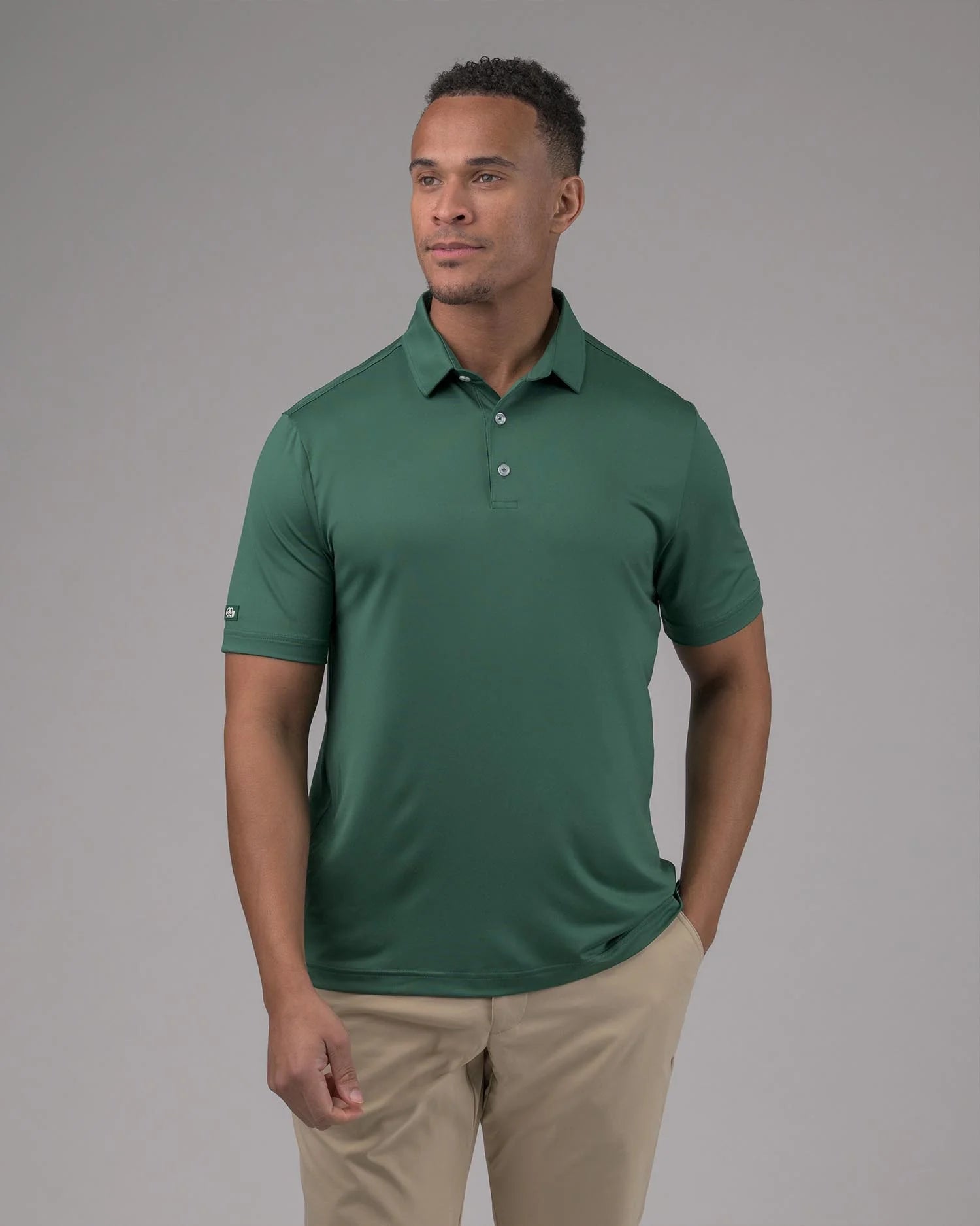 Man wearing a green polo shirt and beige pants against a gray background