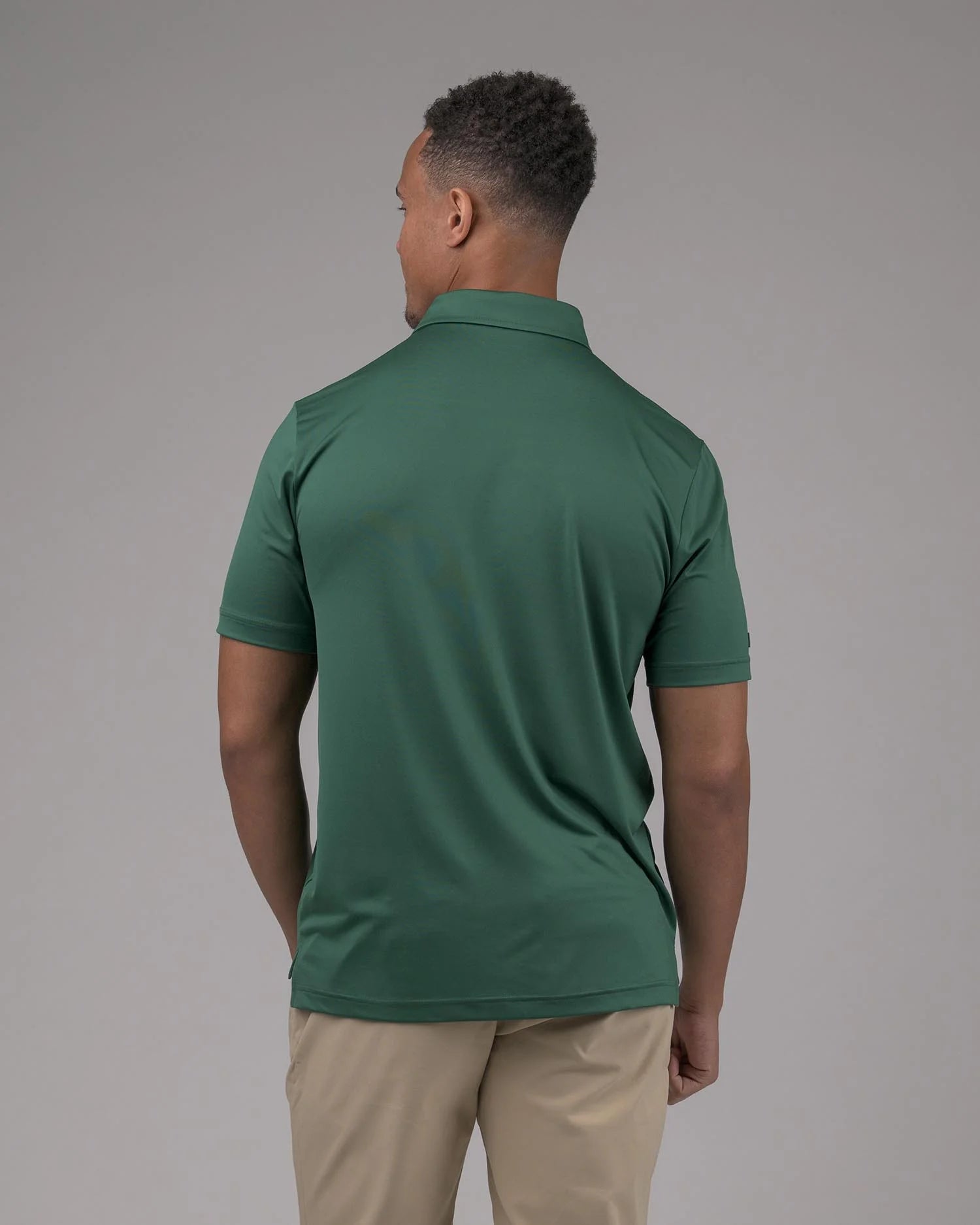 Man wearing a green polo shirt and beige pants against a gray background