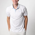 Man wearing a white polo shirt with a logo on a plain background